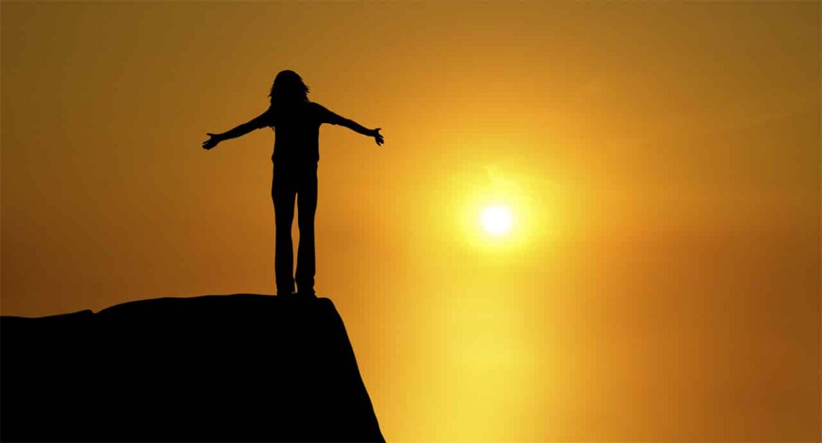 Ein Mensch steht auf einer Bergspitze im Sonnenuntergang