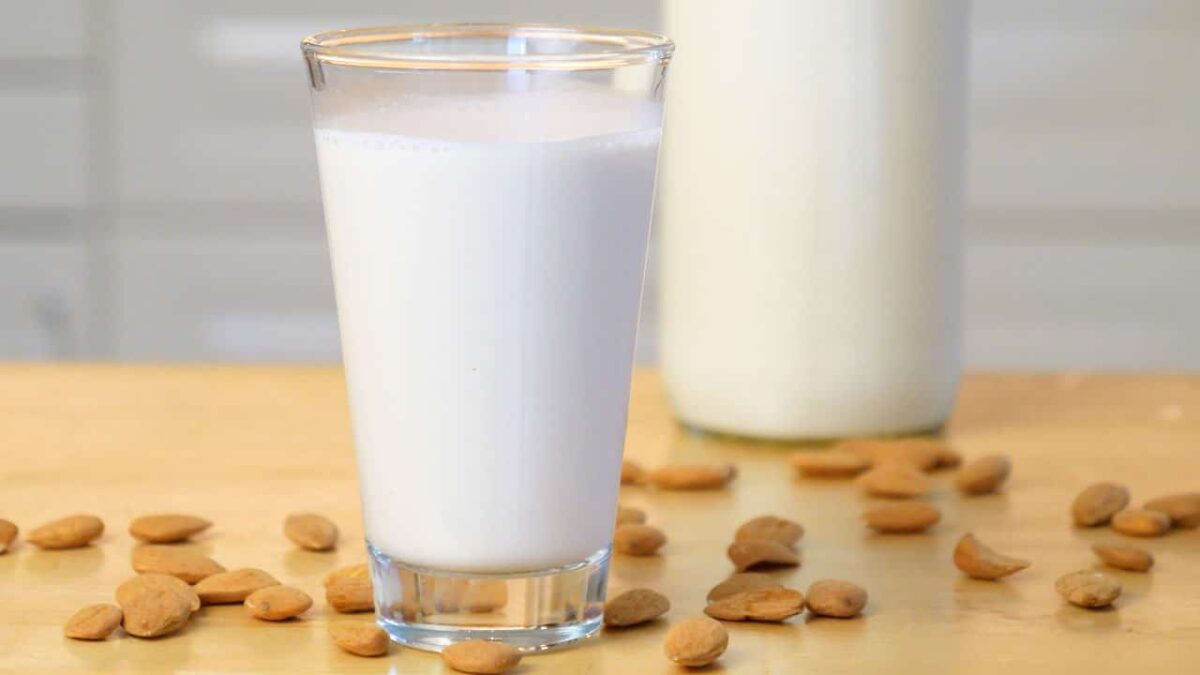 Frisches Glas Mandelmilch auf Holztisch, umhüllt von ganzen Mandeln. Natürlich und köstlich!