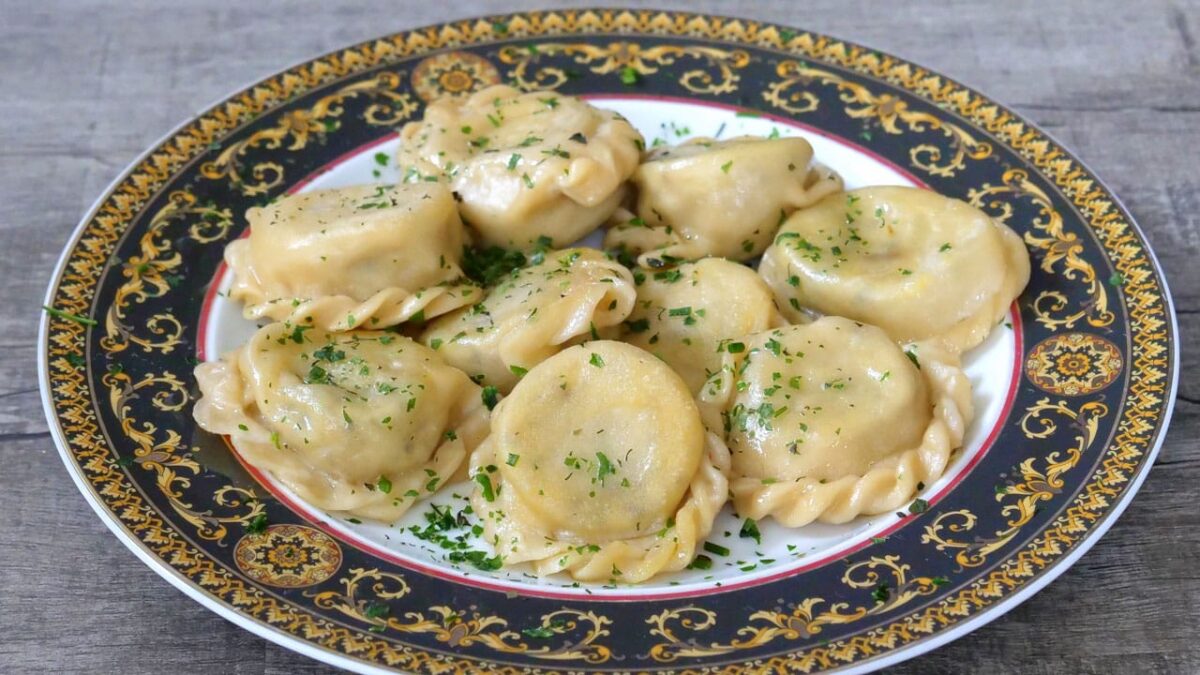 Kärntner Kasnudeln auf kunstvoll verziertem Teller, mit frischen Kräutern garniert.