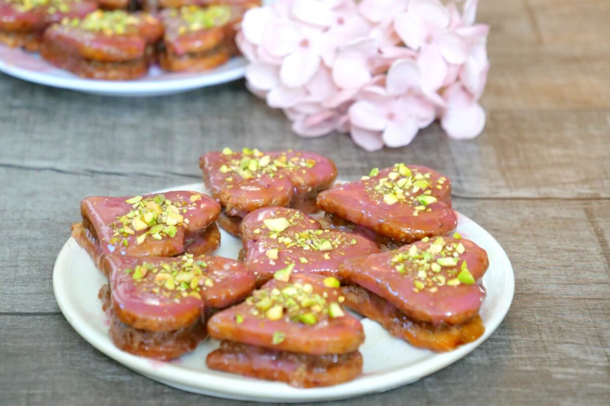 Herzförmige Punschkekse mit rosaroter Glasur und Pistazien, festlich arrangiert.