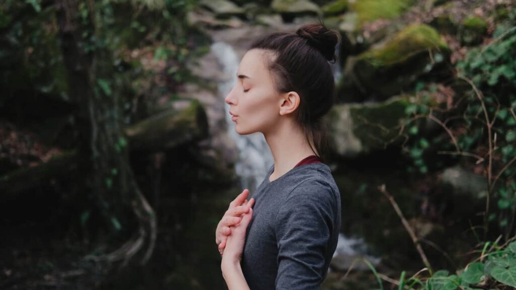 Eine Frau in der Natur die sich die Lunge hält und atmet als Symbol einer Asthma Behandlung