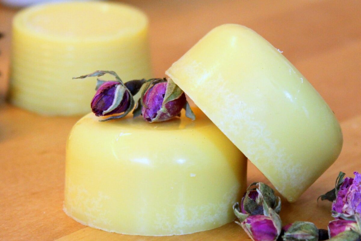 Selbstgemachte Body Melts mit Rosenknospen auf Holz; pflegende Körperbutter.