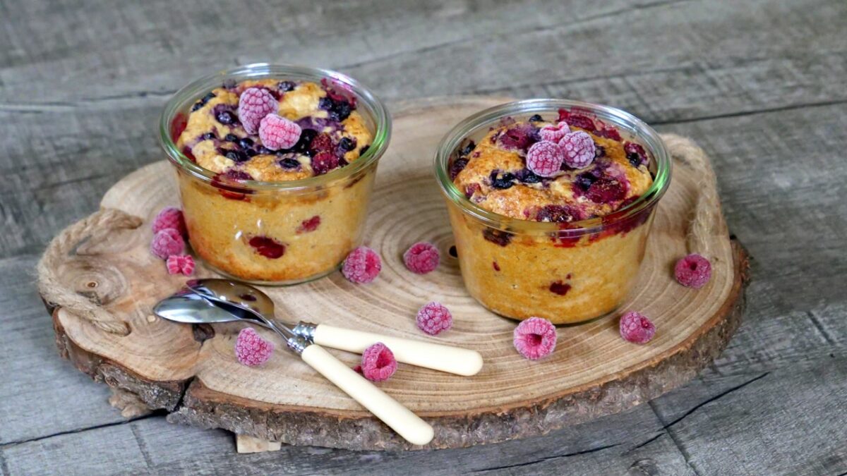 Saftige Beeren-Quarkkuchen im Glas, verführerisch präsentiert auf Holzbrett.