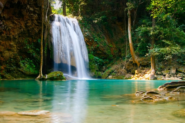 Ein klarer Wasserfall ergießt sich über eine Felskante in ein türkisfarbenes, ruhiges Becken im Wald – ein Ort, der wie ein inneres Tor wirkt, geboren aus Stille, berührt vom Ursprünglichen.