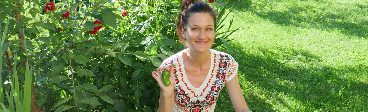 Heilfasten Webinar: Online-Fasten | 7-Tage-Fastenprogramm 3 Sandra Exl sitzt im Garten zwischen Blumen und Gemüse, mit einer frischen Paprika in der Hand – Symbol für Natürlichkeit, Ernährung und Lebensfreude.