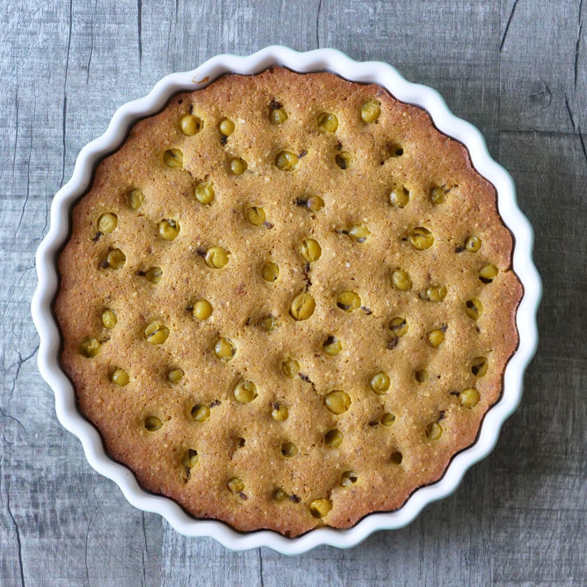 Goldbrauner, glutenfreier Stachelbeerkuchen in geriffelter Form auf rustikalem Holz. Schmackhaft und einladend.