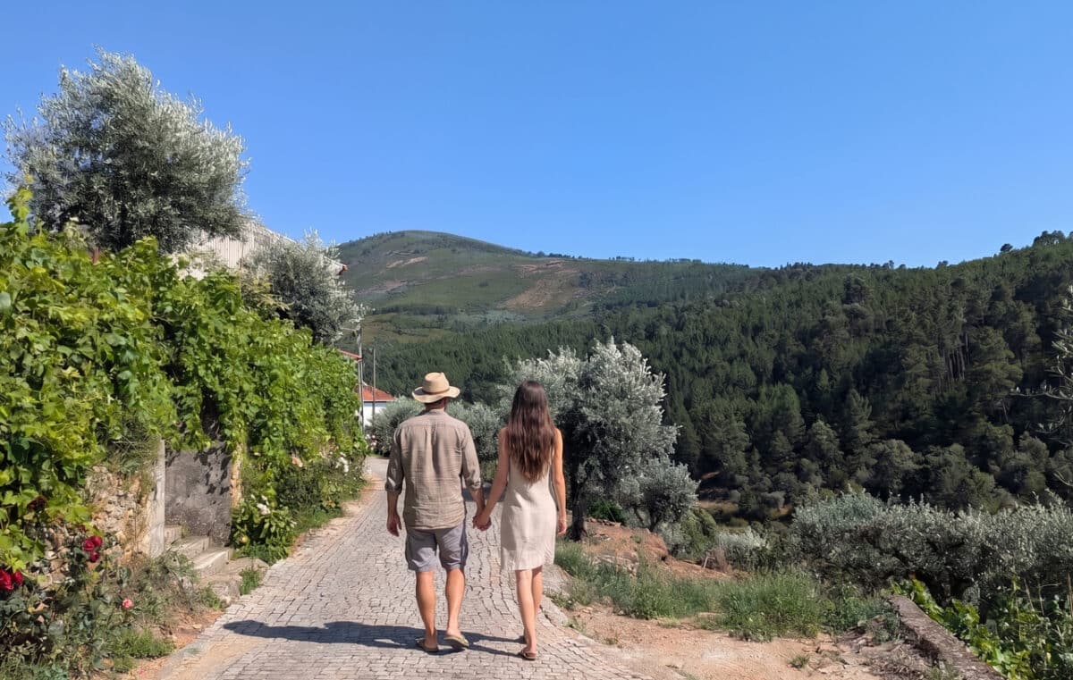 Ein Paar geht Hand in Hand einen gepflasterten Weg in einer hügeligen, grünen Landschaft in Portugal entlang